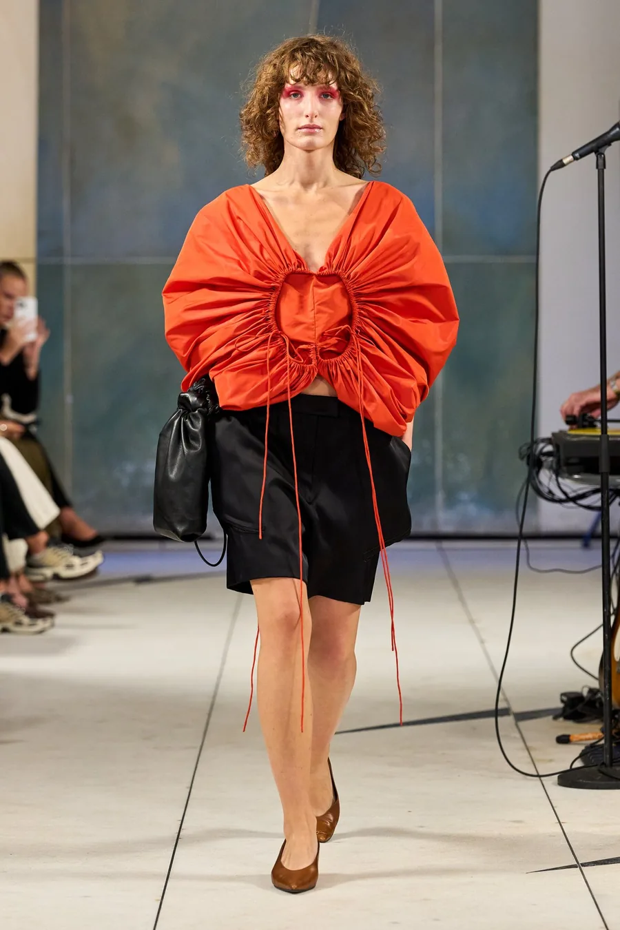 SHOWstudio, Litkovska S/S 27 STRICHA: modelo con una blusa naranja fruncida y pantalón corto negro con cintas largas